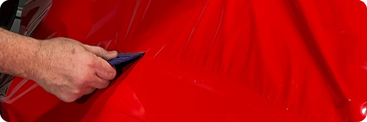 Installer using a squeegee to apply Briteline ColorCAST Crimson Crush color change vinyl wrap to a vehicle panel